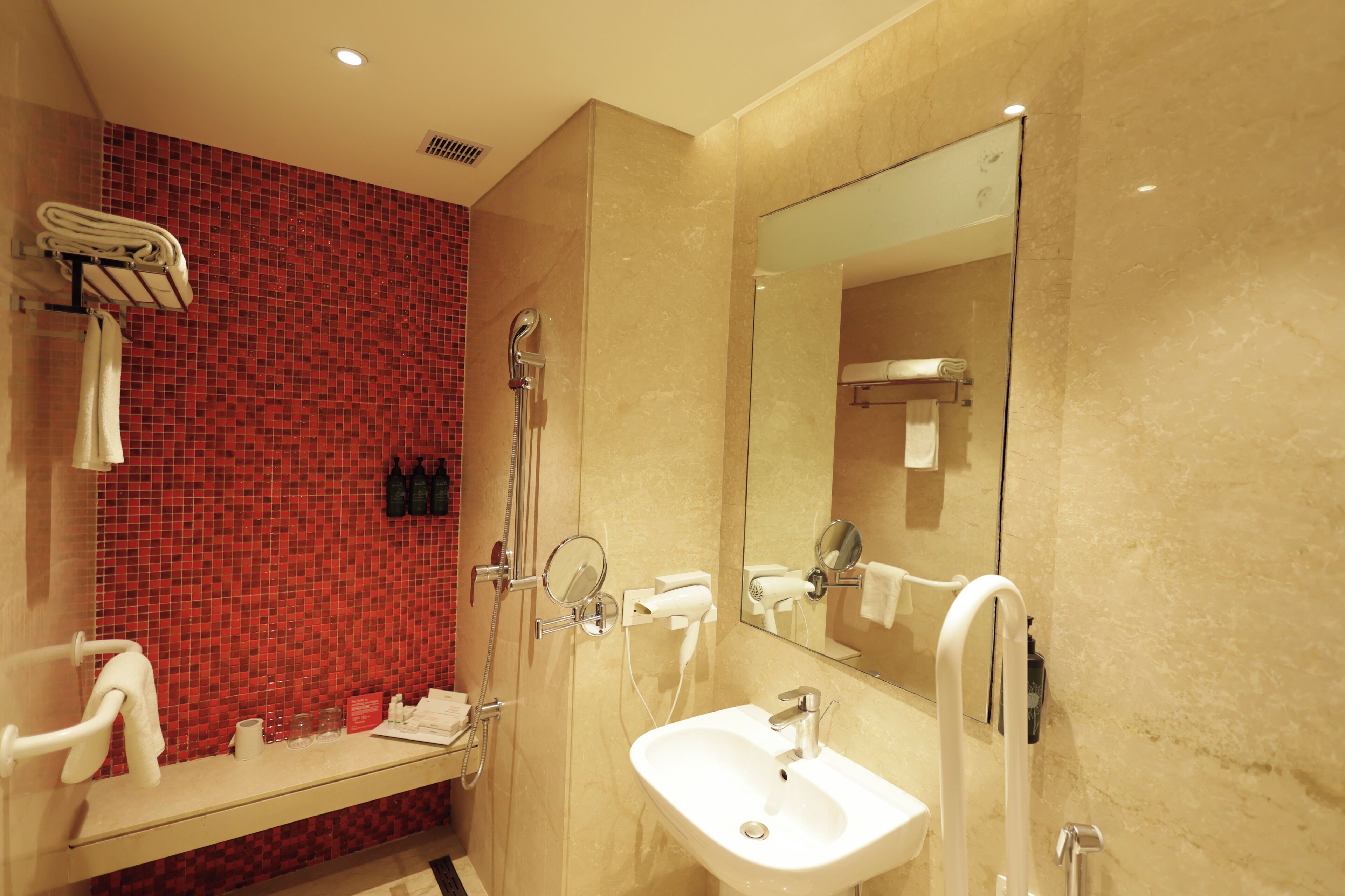A modern bathroom with a red mosaic wall, a sink, a mirror, and a shower.