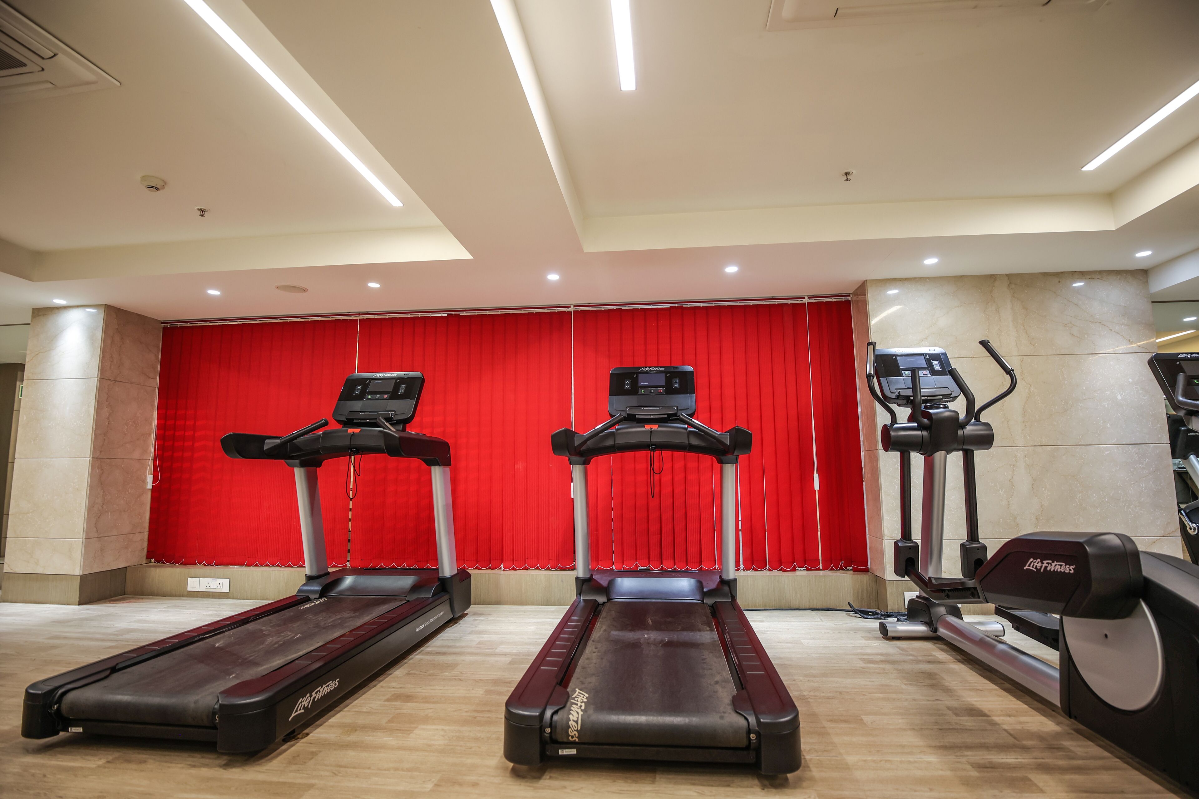 Un gimnasio con cintas de correr y elípticas, un telón rojo de fondo y suelo de baldosas.