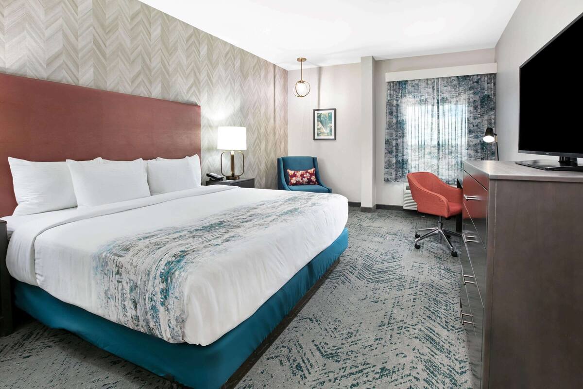 A hotel room with a large bed, a desk with a chair, a television, and a window with curtains.