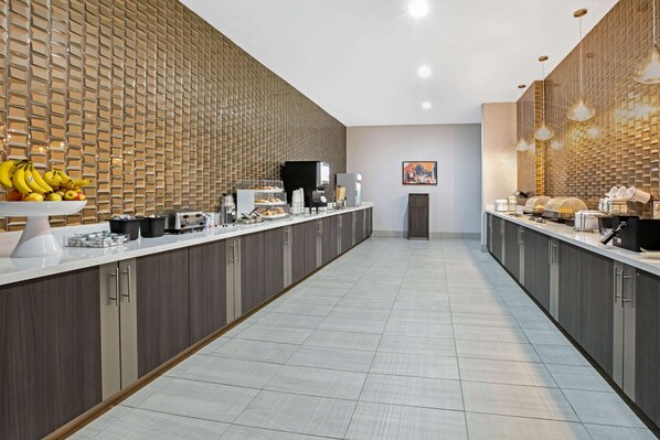 A modern kitchen with a long counter, equipped with coffee machines, a refrigerator, and a microwave.