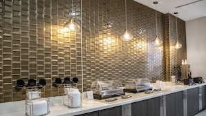 A modern breakfast bar with a patterned backsplash, buffet setup, and pendant lighting.