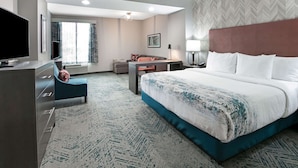 A hotel room with a large bed, a desk, a television, and a seating area with a chair and a sofa.