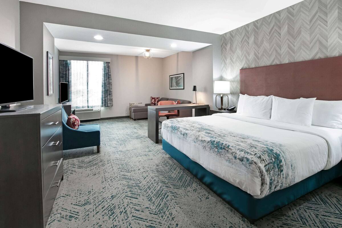 A hotel room with a large bed, a desk, a television, and a seating area with a chair and a sofa.