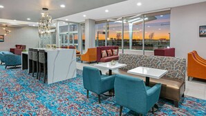 A modern hotel lobby with a bar area, seating arrangements, and large windows offering a view of the sunset.