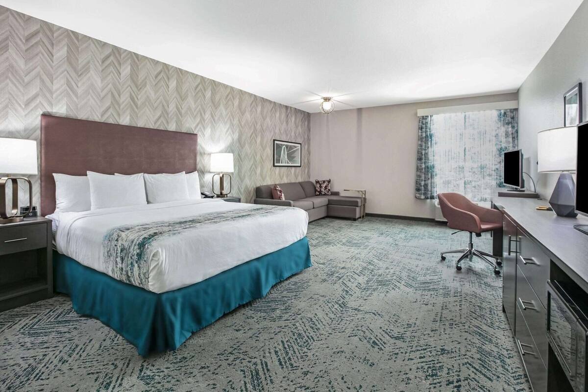 A hotel room with a bed, a desk, a chair, a sofa, and a television.
