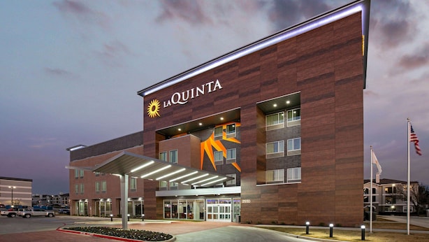 A La Quinta hotel with a modern design, featuring a prominent logo and a large entrance with a covered walkway.