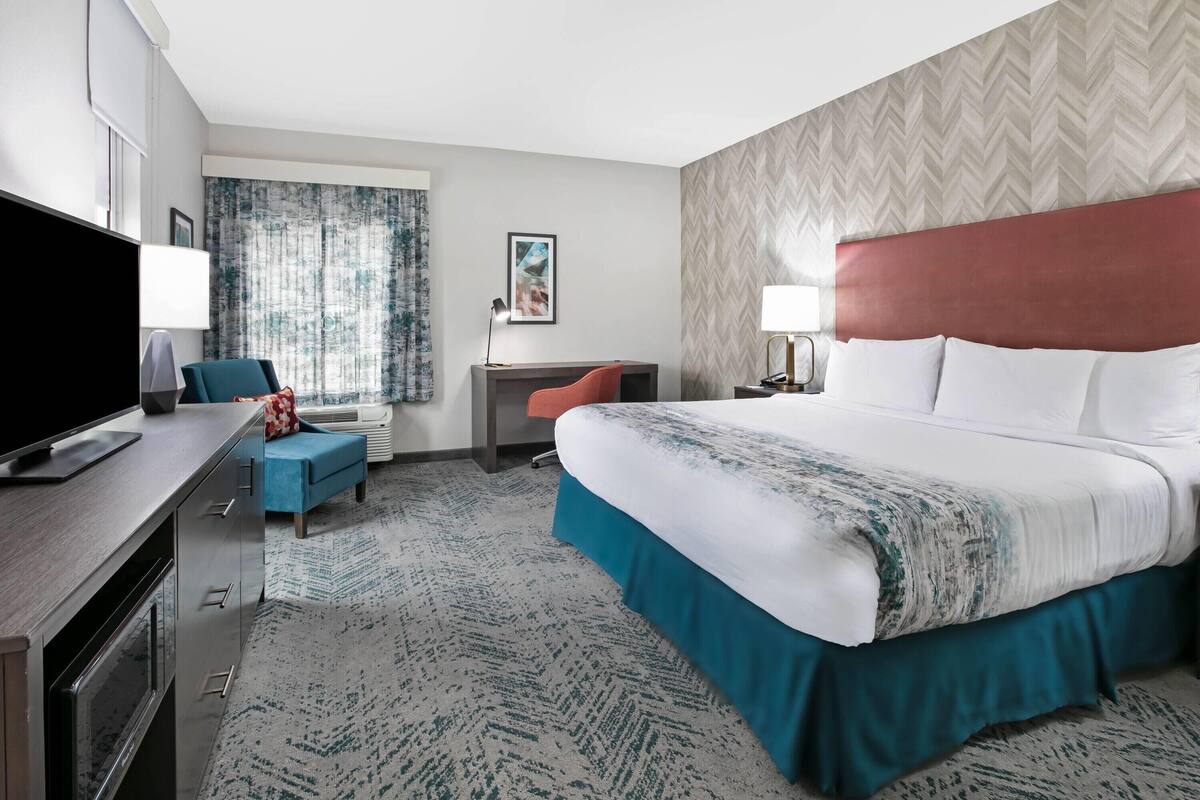 A hotel room with a bed, desk, chair, television, and a window with curtains.