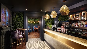 Un espace bar doté d’un comptoir en bois, de luminaires hexagonaux suspendus et de différentes bouteilles et verres exposés sur des étagères.