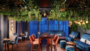 Un espace lounge moderne avec une table en bois, des tabourets de bar, des canapés et un fond de scène constitué d’un rideau bleu.