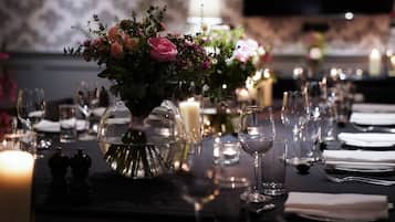 Ein Esstisch, gedeckt mit Kerzen, Gläsern und einer Blumenarrangements als Mittelstück.