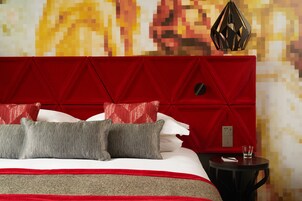 A bed with a red headboard, grey and red pillows, and a small bedside table with a glass.