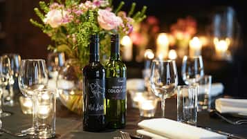 Mesa preparada para cenar con botellas de vino, copas y un centro de mesa floral.