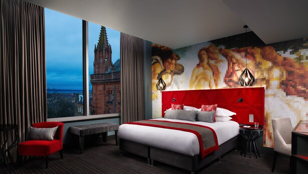 Une chambre d’hôtel avec un grand lit, une tête de lit rouge, une vue sur un bâtiment historique et une fresque murale contemporaine.