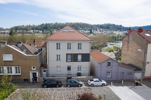 A multi-story residential building with a red-tiled roof, a central entrance, and a small parking area with three cars.