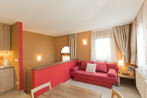 A compact living space with a red sofa, a wooden dining table, and a kitchenette area.