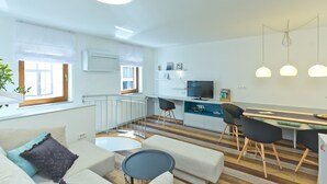 A modern apartment with a living room, dining area, and kitchen. It features a large window, a flat-screen TV, and a dining table with chairs. - City Centre Apartments (Ljubljana)