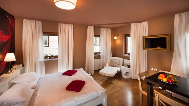A hotel room with a bed, a desk with a fruit bowl, a chair, a TV, and a window with curtains. - City Centre Apartments (Ljubljana)