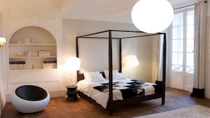 Een hemelbed met witte beddengoed en een sprei, met aan beide zijden nachtlampen.
