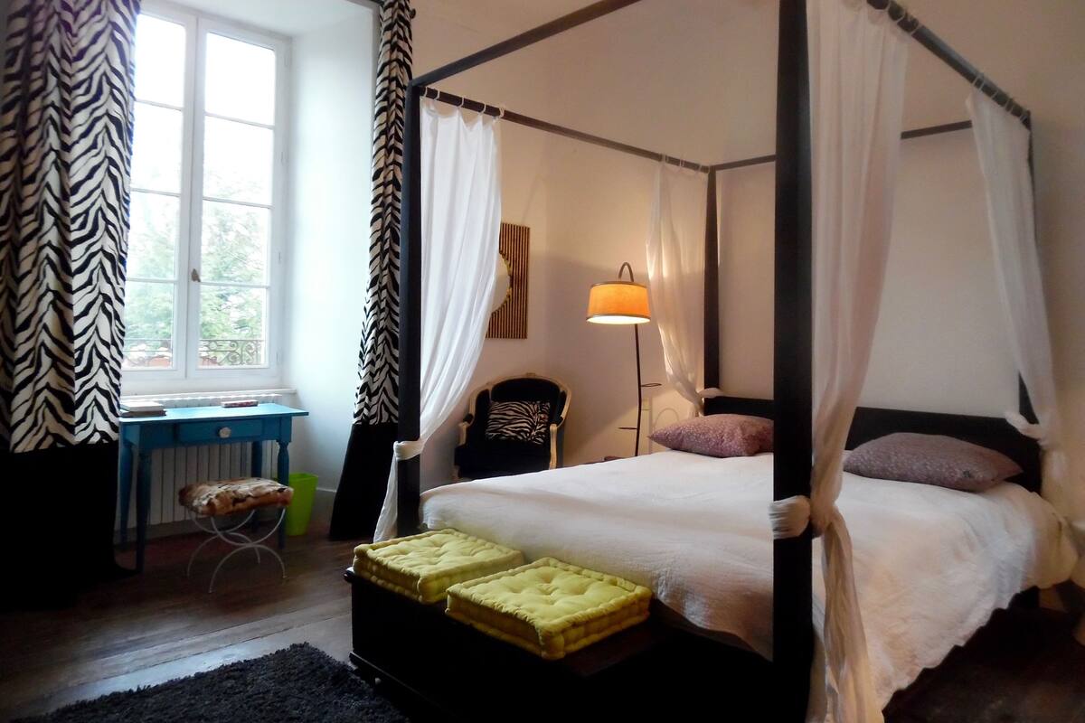 Un lit à baldaquin avec une literie blanche, une lampe de chevet et une chaise avec un coussin.