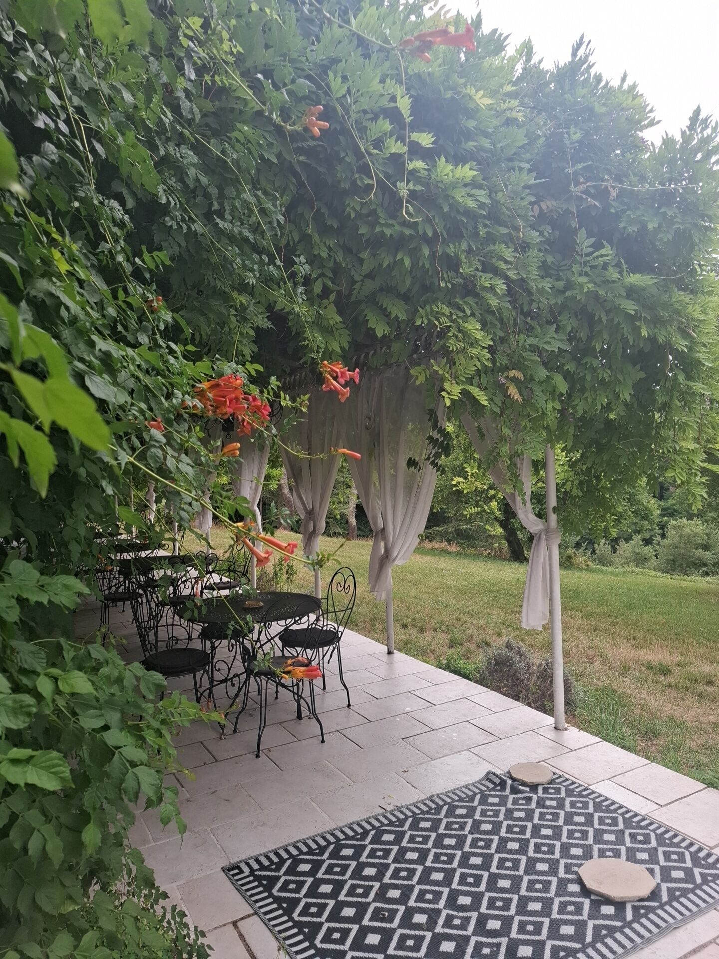 An outdoor patio with a patterned rug, metal chairs, and a table.