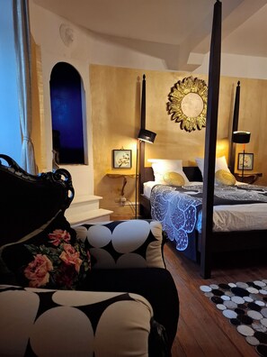 Una cama con dosel con un edredón estampado en azul y blanco, una mesita de noche con lámpara y un espejo con marco dorado fijado a la pared.