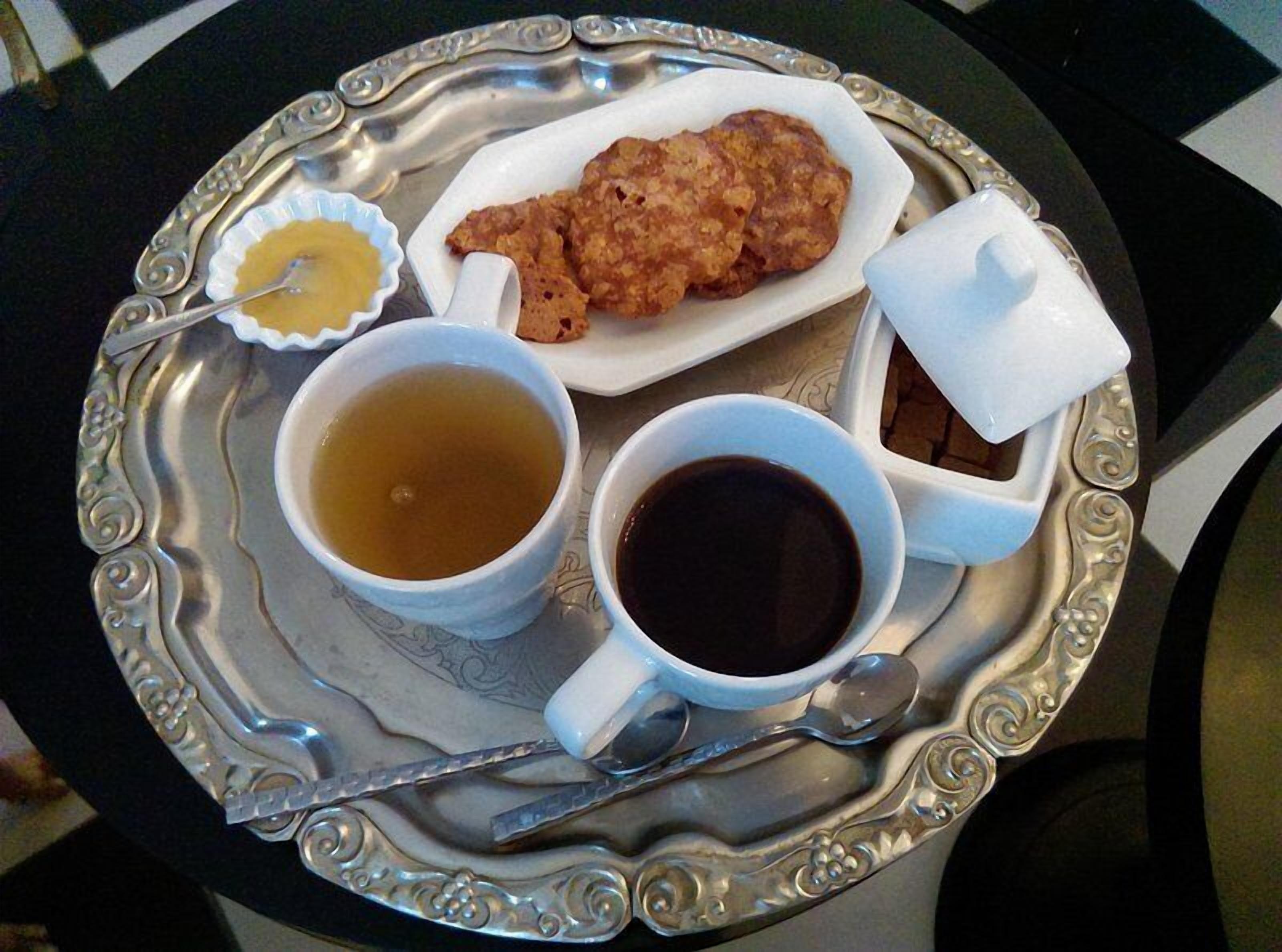A tray with two cups of tea, a small bowl of jam, and a container of sugar.