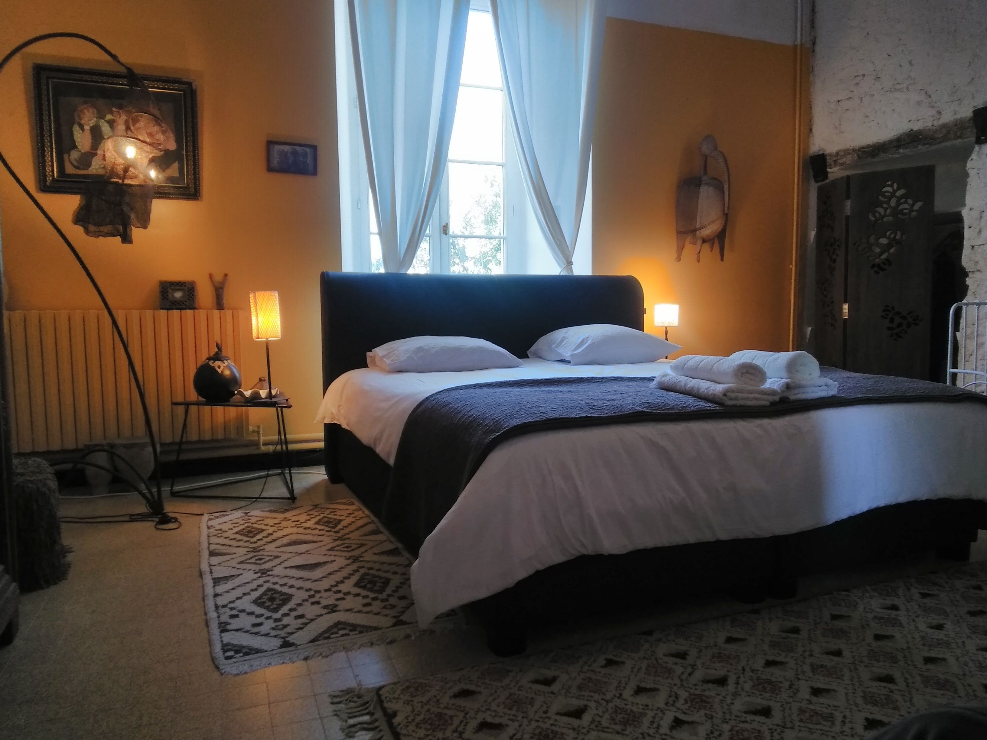 Un dormitorio con una cama grande, un radiador, una lámpara y una ventana con cortinas.