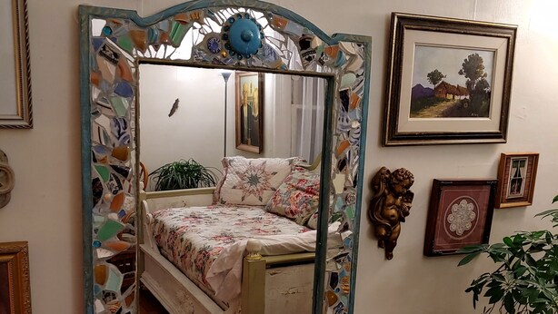 A bedroom with a bed, a mirror, and various framed pictures on the wall.