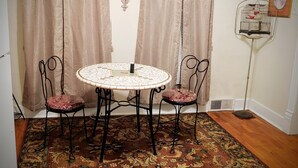 A room with a round table and four chairs, a patterned rug, curtains, and a birdcage on the wall.