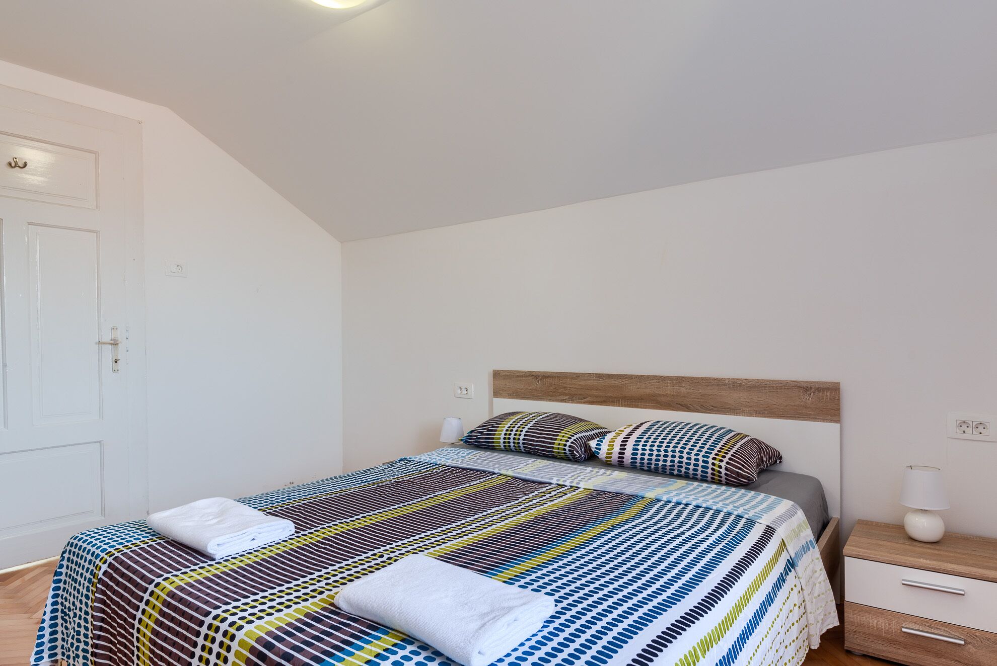 Un dormitorio con cama, mesita de noche, lámpara y puerta.