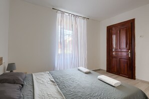 A bedroom with a bed, a wooden door, and a window with curtains.