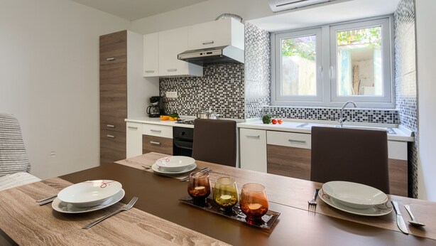 A modern kitchen with white cabinets, a black and white tiled backsplash, and a window with a view of greenery. - Andrea&Leon Apartments (Mali Losinj)