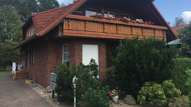 Una casa de dos pisos con techo de tejas rojas, un balcón con jardineras y fachada de ladrillo.