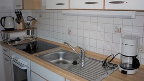 Una cocina con armarios blancos, un lavamanos de acero inoxidable, una cafetera y un hervidor.