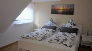 Un dormitorio con techo inclinado, una cama con ropa de cama floral, una mesita de noche y un cuadro de una puesta de sol.