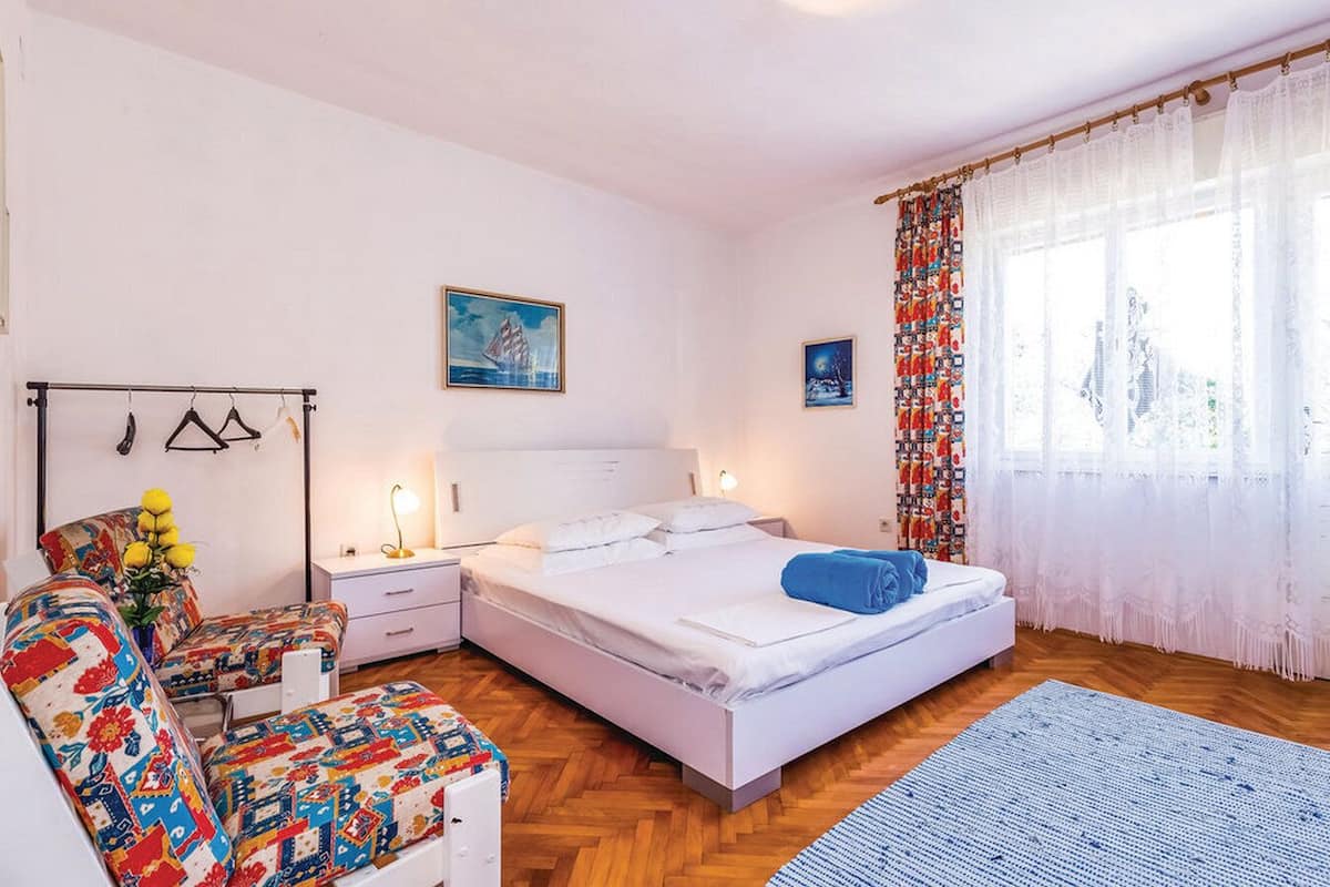 Een slaapkamer met een bed, nachtkastjes, een stoel, een bureau en een raam met gordijnen.
