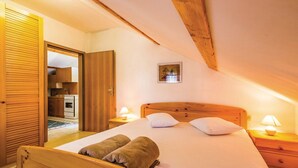 Een slaapkamer met een houten bed, twee bedlampen, een houten hoofdbord en een deur naar een keuken.