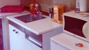 A compact kitchen with white cabinets, a stainless steel sink, a microwave, and a small oven. - Barac Apartments (Novi Vinodolski)
