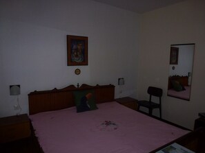 A bedroom with a wooden bed, a pink bedspread, a nightstand with a lamp, a chair, and a mirror on the wall. - Barac Apartments (Novi Vinodolski)