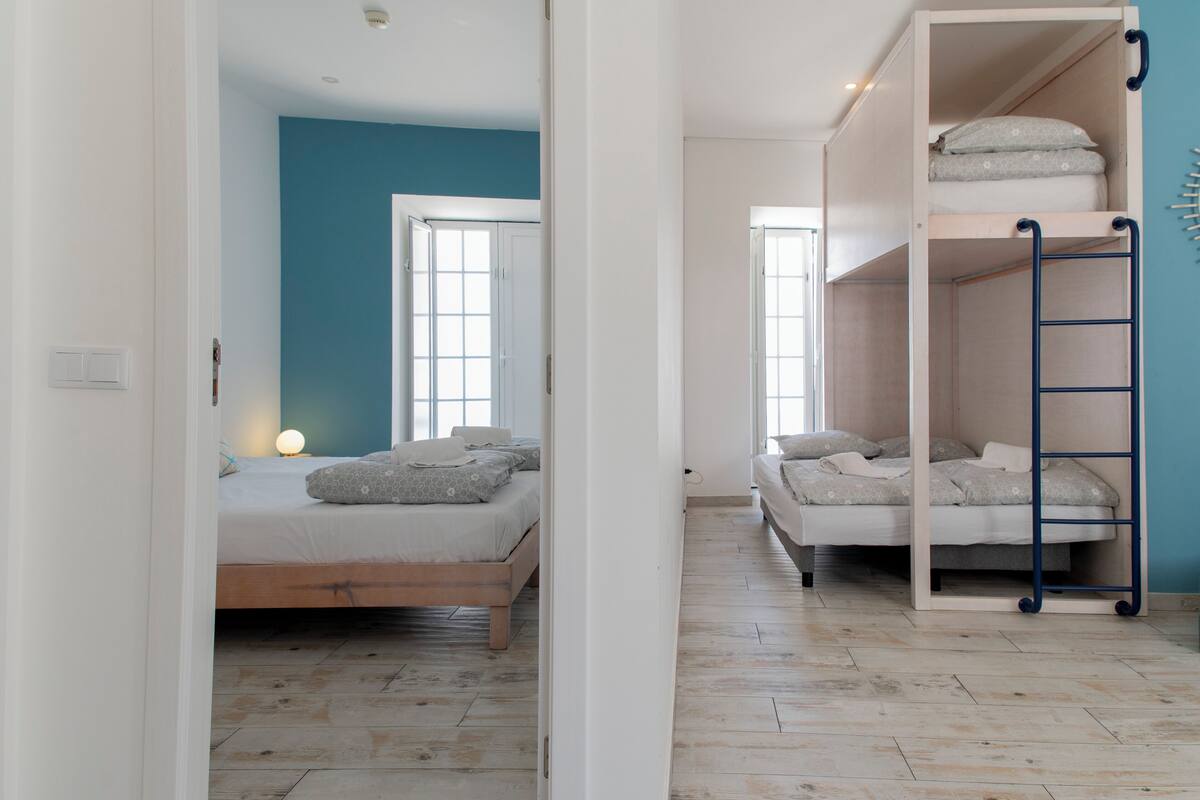 A room with a bunk bed, a single bed, and a window.