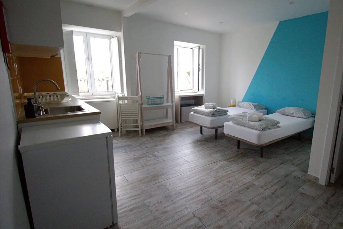 A compact bedroom with a bed, a small desk, and a kitchenette.