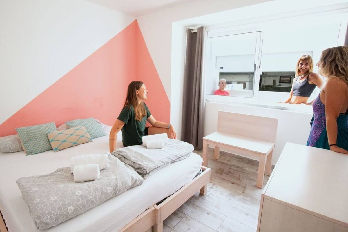 A modern bedroom with a bed, pillows, a bench, and a view of a balcony.