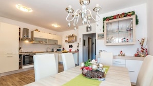 A modern kitchen with white cabinets, a microwave, and a dining area with a table set for two. - Apartments Franjkovic (Novi Vinodolski)