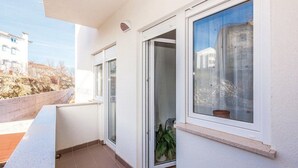 A balcony with a sliding glass door, a potted plant, and a view of a building across the street. - Apartments Franjkovic (Novi Vinodolski)