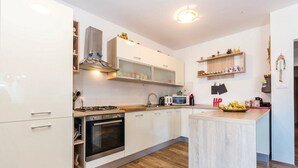 A modern kitchen with white cabinetry, a central island, and wooden flooring. - Apartments Franjkovic (Novi Vinodolski)