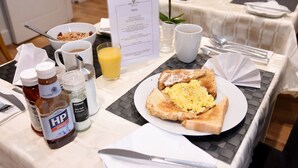 A breakfast table with a menu, a bowl of cereal, a glass of orange juice, a plate with toast and scrambled eggs, and condiments. - Apple Tree Place B&B (Tadley)