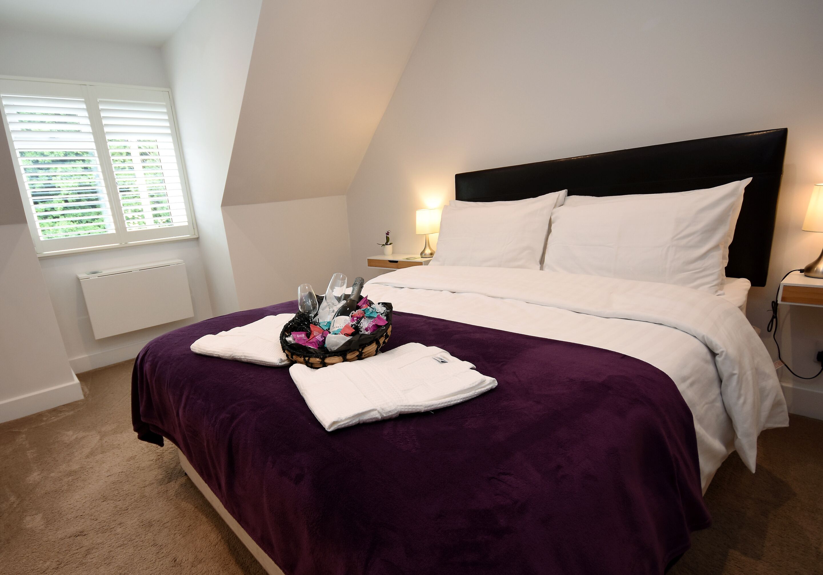 A bedroom with a bed, a window, a nightstand, and a lamp.