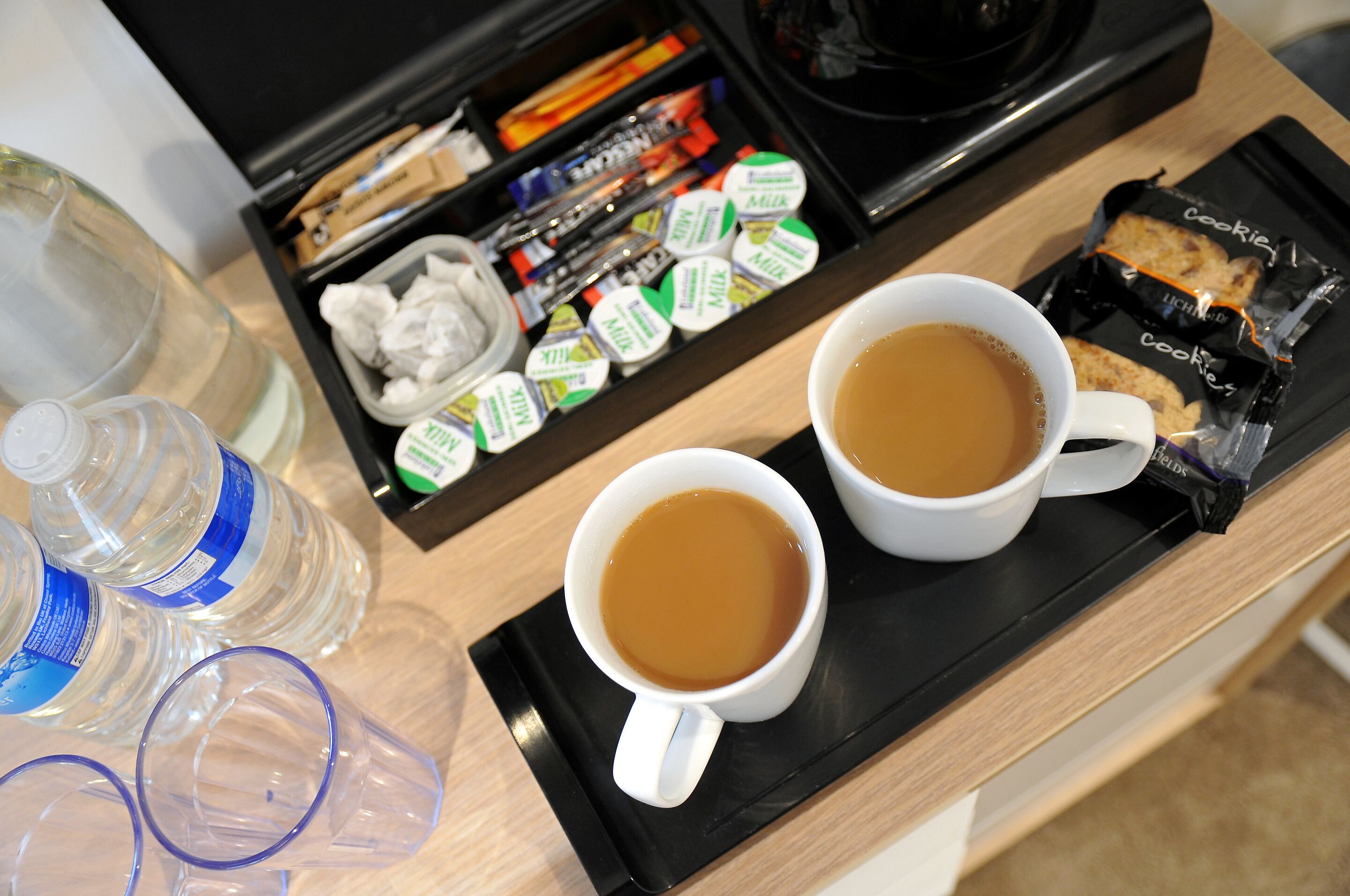 Una bandeja con dos tazas de café blancas, una botella de agua y un envase de cartones de leche.