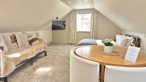 A cozy room with a sofa, a small table, and a TV mounted on the wall. - Apple Tree Place B&B (Tadley)