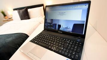 Una laptop sobre una cama con una colcha blanca y almohadas negras.